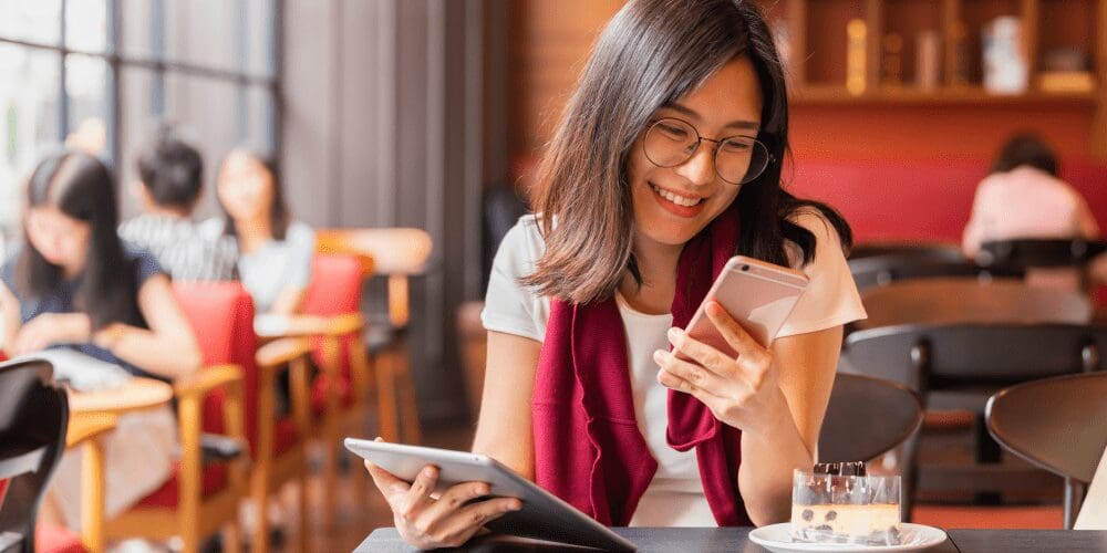 Young woman at a coffee shop smiling at her devices