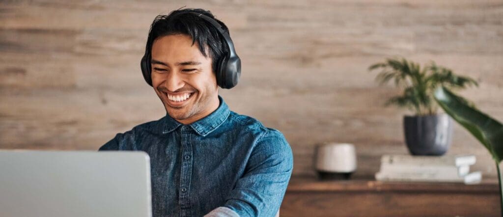 man with headphones smiling at his computer