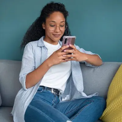 Smiling Woman Using Her Mobile Phone While Sitting on Sofa