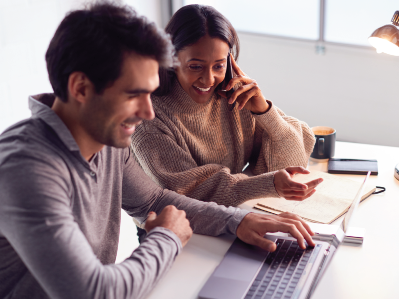 A man and woman sitting at a desk with a laptop