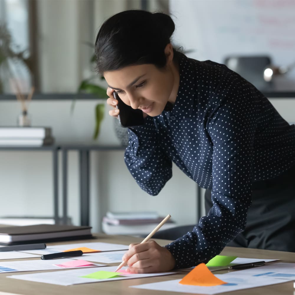 Businesswoman Talking on Cellphone, Writing Notes on Colorful Sticky Notes in Office