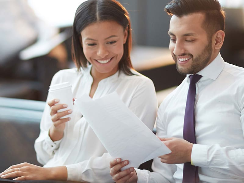 Man and woman in business attire drinking coffee and reviewing compliance document