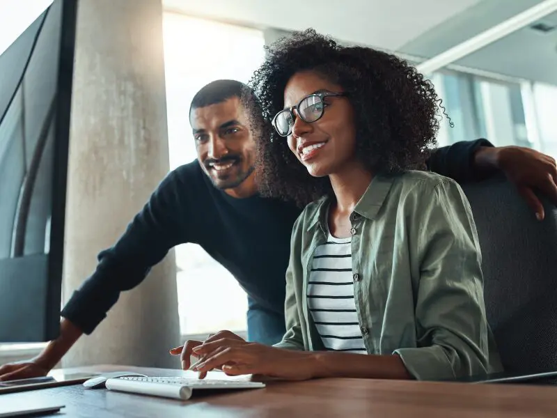 Office workers smiling while discussing something they are looking at on the computer.