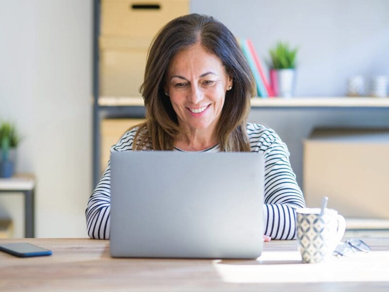 Woman smiling at a computer with sunlight coming in the window.