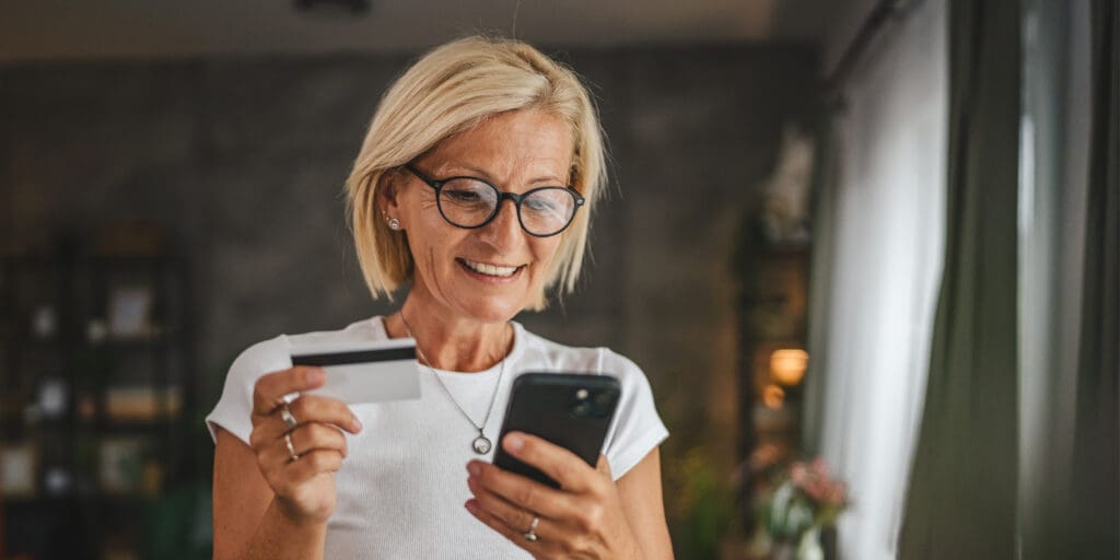 Portrait of a Smiling Woman Standing and Buying Items Online Using Cellphone With Credit Card