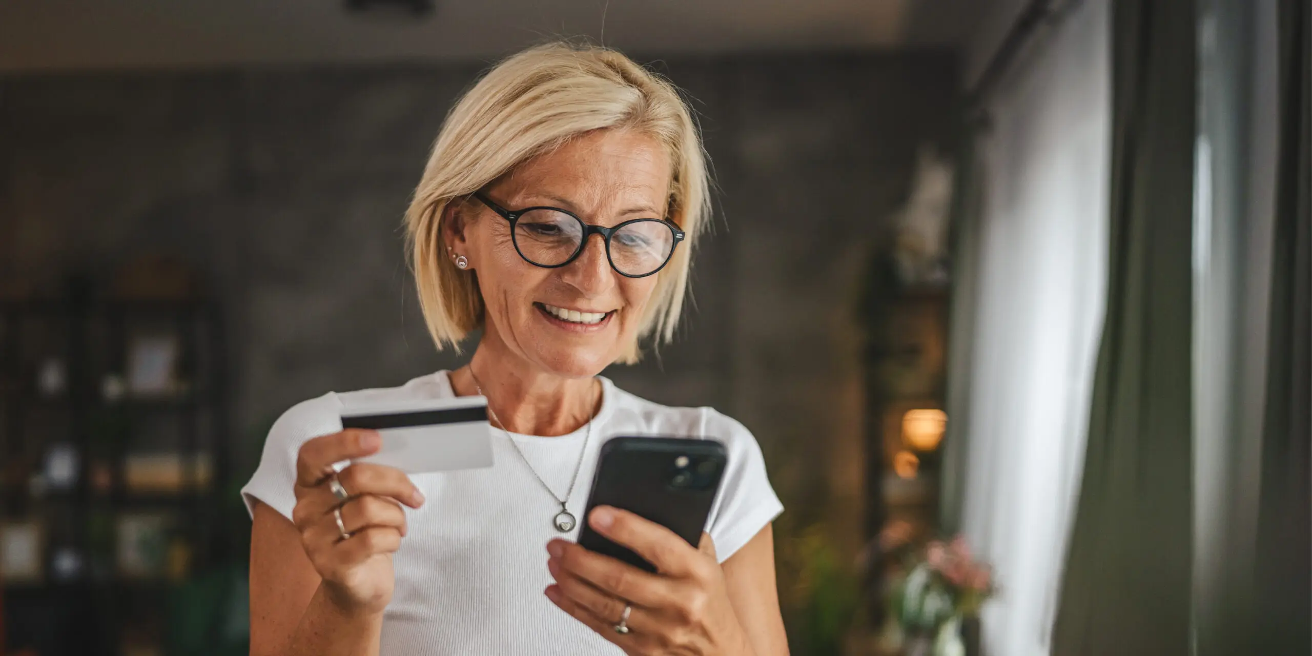 Portrait of a Smiling Woman Standing and Buying Items Online Using Cellphone With Credit Card