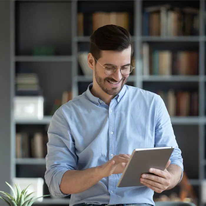 Smiling Businessman Wearing Glasses Using a Tablet and Standing in Modern Office