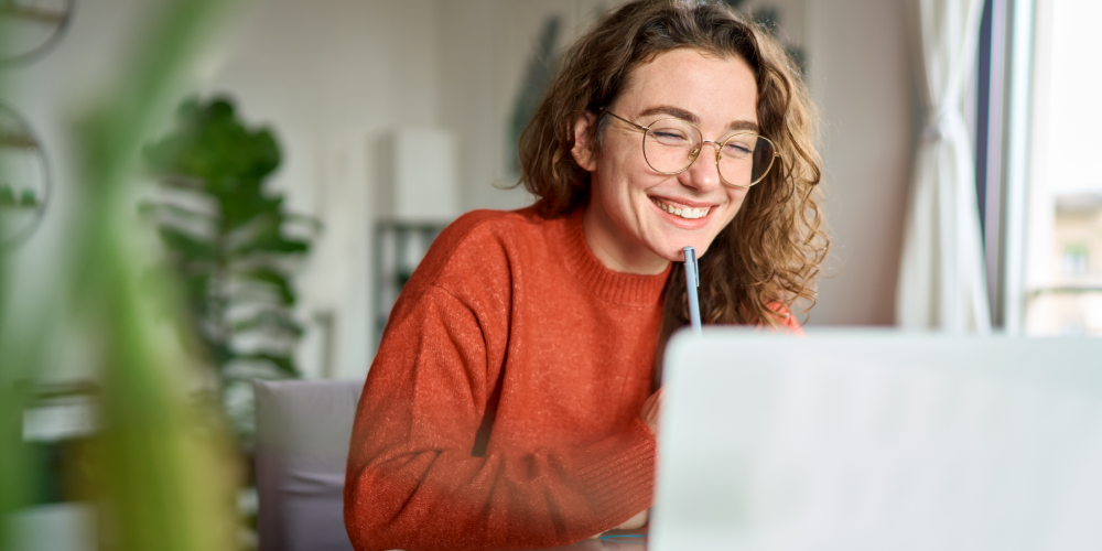 Woman holding a pen smiling at a computer screen