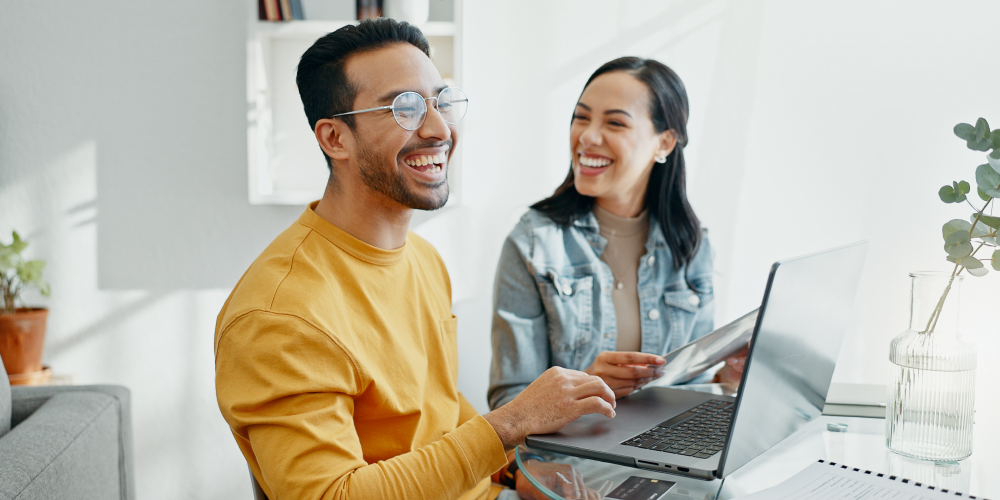 A smiling man and woman engage with a laptop, reflecting a positive and collaborative atmosphere.