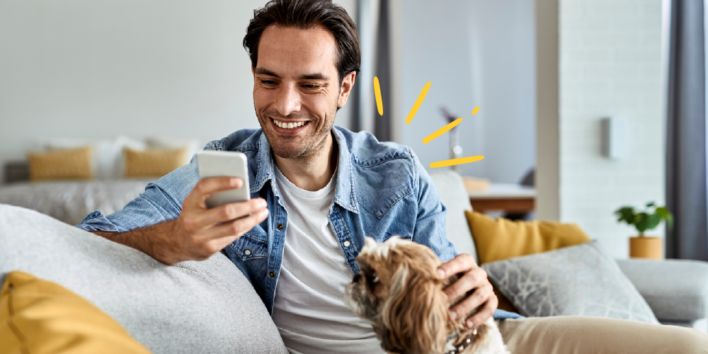 A man sits comfortably on a couch with his dog, engaged with his cell phone, sharing a peaceful moment at home.