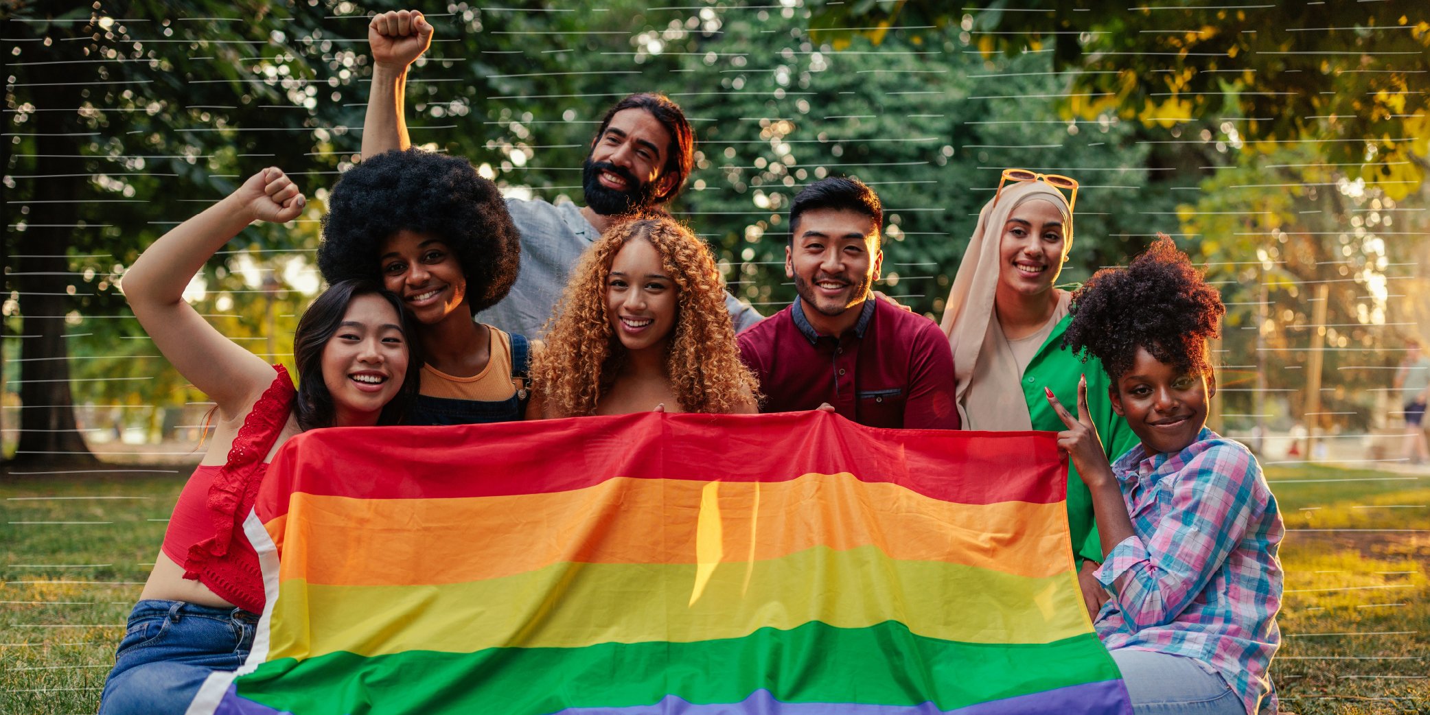 A Group of Gay Rights Activists Are Sitting on the Grass Lawn Outdoors With a Pride Flag Supporting Pride Month