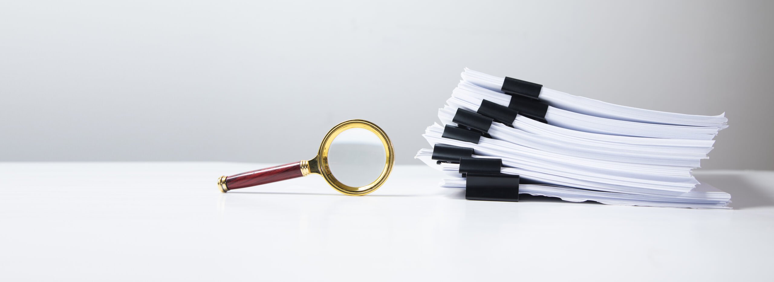 Stack of report paper documents with magnifying glass.